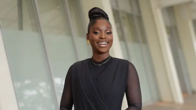Tomike Adeoye smiling for the camera - she is wearing a black dress with a necklace around her neck.