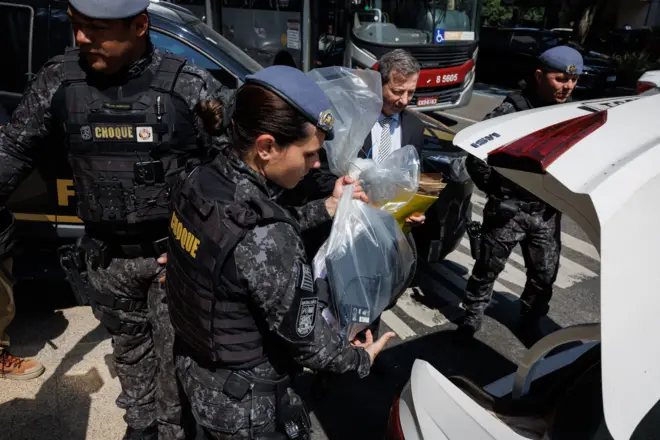 Policial fazendo apreensão e colocando sacola em carro