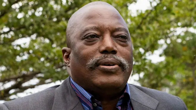 Joseph Kabila naa ree to ya fọto niwaju igi kan, o wọ aṣọ oyinbo alawọ eeru, o si wọ omin-in to ni awọ omi aro ati ila tẹẹrẹ sinu.