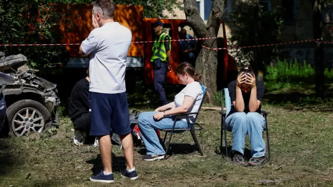 Ljudi sede ili stoje i drže se za glavu ili rukama pokrivaju lice napolju posle ruskih udara na Kijev