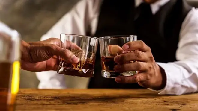 دست‌های دو مرد که هر کدام لیوانی از الکل در دست دارند