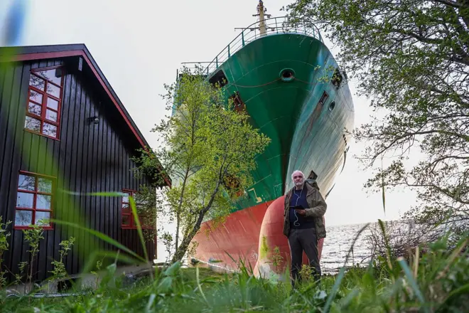 Johan Helberg en la puerta de su casa con el barco detrás.