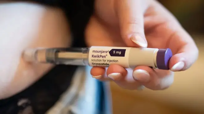 A hand holding a jab on which a labelled as Mounjaro, a solution of tirzepatide for injection, pointing into the skin