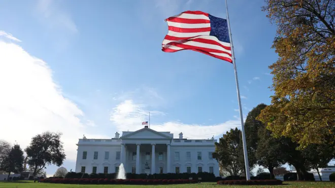 Флаг США развевается на фоне Белого дома.