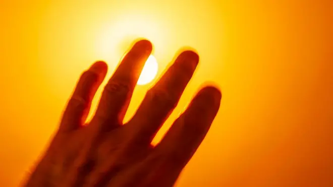 Mano borrosa por la intensidad de la luz del Sol, que está detrás de ella. La imagen es de tonos amarillos y naranja
