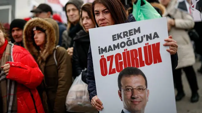 Kalabalık bir alanda bir kadın Ekrem İmamoğlu'na Özgürlük yazılı pankart tutuyor.