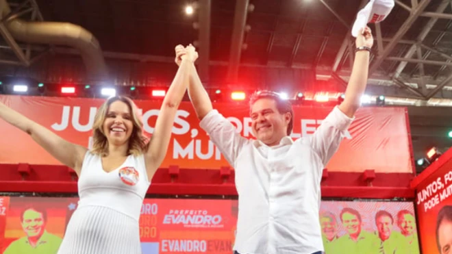 Prefeitojogo de desenharFortaleza, Evandro Leitão, comemorando vitória, com as mãos para o alto com mulher loira. Ambos sorriem