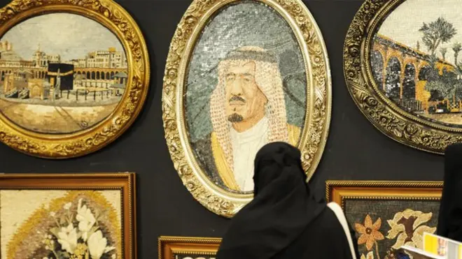 امرأة سعودية تنظر إلى لوحة للملك السعودي