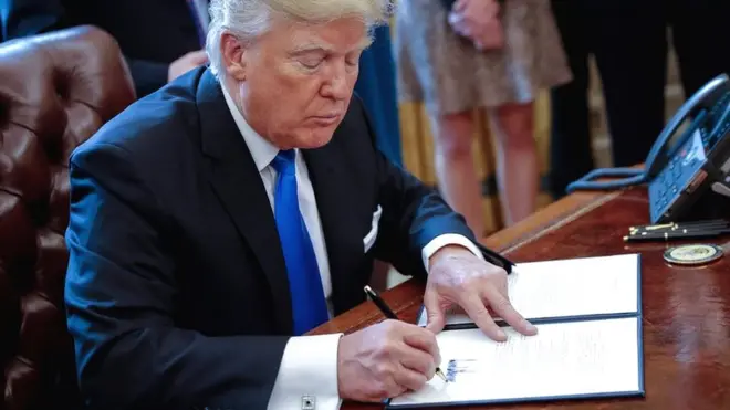 Esta foto tomada en la oficina oval de la Casa Blanca, se ve a Trump firmando una orden ejecutiva.