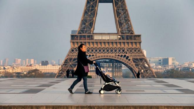 امرأة تسير وهي تجر عربة ابنها أمام برج ايفيل في باريس