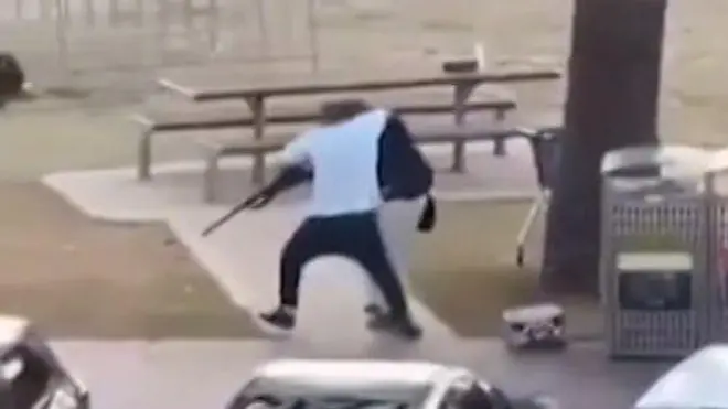 Ifoto igaragaza umugabo wambaye umupira w'umweru w'amaboko magufi arimo kwambura imbunda urimo kurasa. 