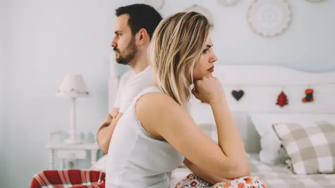 Mulher e homem sentados na cama, pensando (stock photo)