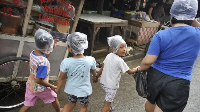 An Indonesian woman with three children wears a plastic bags over their heads to protect from light rain at a Jakarta market on February 04, 2011.