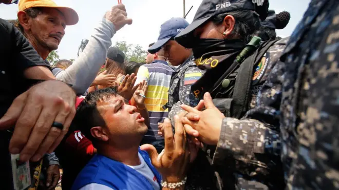 A supporter kneels in front of Bolivar state security forces