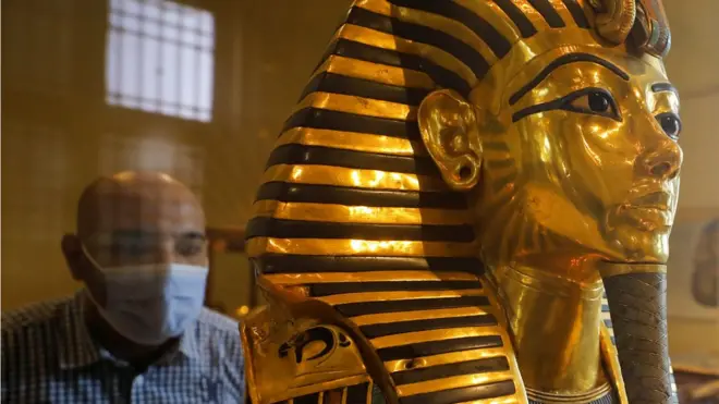 شخص يرتدي كمامة يطالع قناع توت عنخ آمون الذهبي