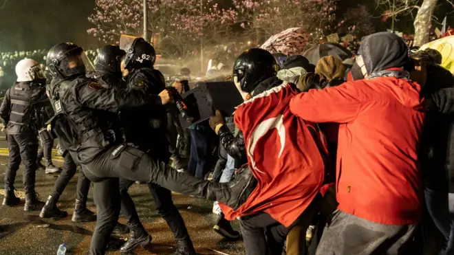 An armoured riot police officer can be seen kicking out at a man wearing a Turkish flag