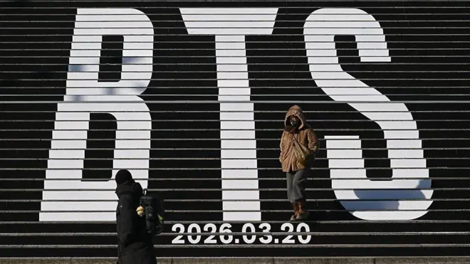 Pedestrians walk along the stairs displayed with the BTS logo and release date of BTS' 2026 album at Gwanghwamun Square in Seoul on January 14, 2026.