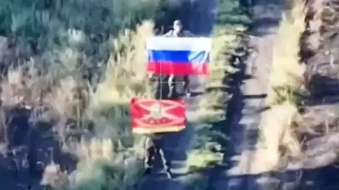 A fuzzy image of two men holding Russian flags on a road - one of the flags is a tricolour the other is a red military flag