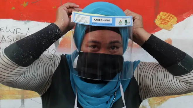 Seorang warga Surabaya memakai alat pelindung wajah (face shield) yang didapat dari pembagian Alat Pelindung Diri (APD) di Pasar Keputih, Surabaya, Jawa Timur, Minggu (28/06)