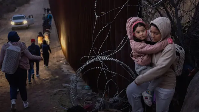 Mujer cruzando a la frontera con su hija en brazos