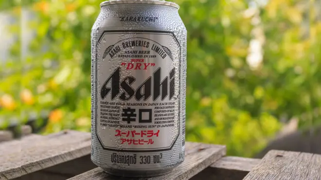 Close up of silver Asahi beer can on wooden outdoor table and natural green foliage in background 