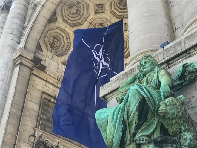 علم حلف شمال الأطلسي NATO يرفرف في مهب الريح تحت أروقة متنزه سينكونتينيير في بروكسل