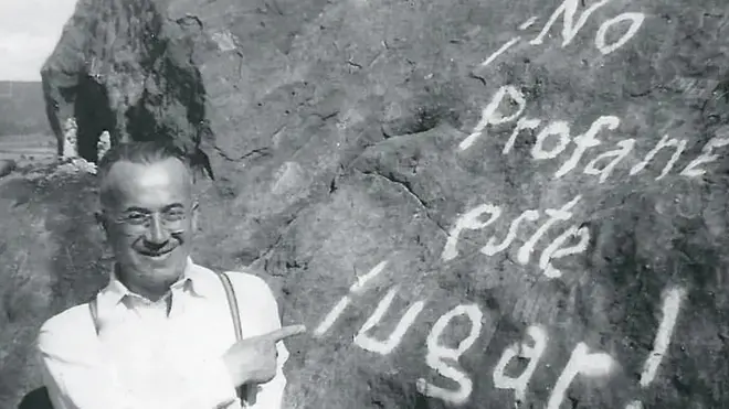 Gonzalo Rojas de joven en una imagen en blanco y negro, junto a una piedra que tiene una inscripción con pintura que pone "¡No profane este lugar!"