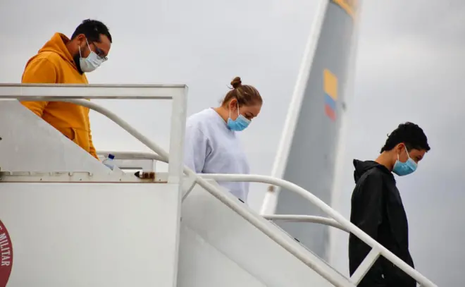 Três pessoas com máscaras faciais descendo de escada de avião