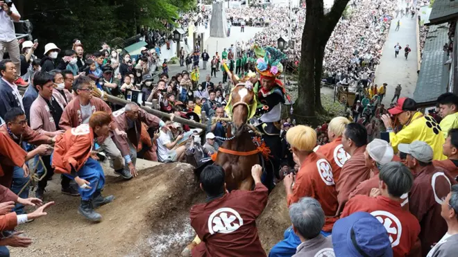 A horse and rider climb a steep clay wall surrounded by crowds at this year's Ageuma Shinji or Rising Horse Festival