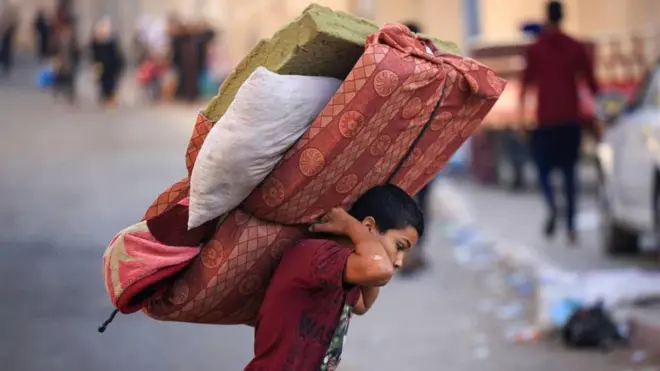 Um menor palestino carregando um colchão nas costas