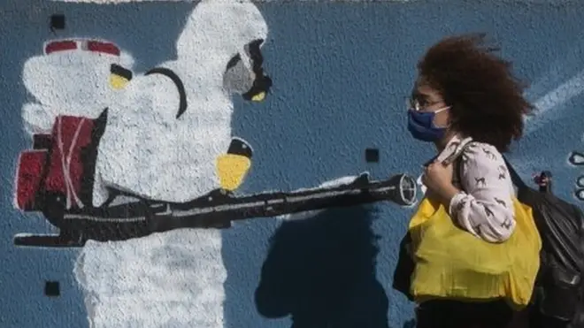 Mulher caminha diante de grafiti no Rio