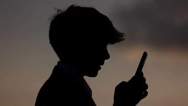 Профиль 13-летнего подростка, который смотрит в экран смартфона