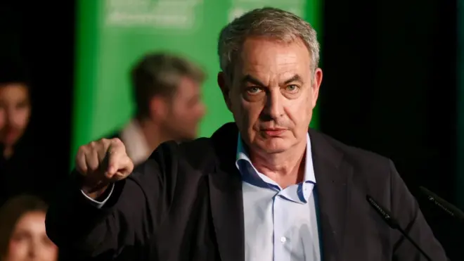 El expresidente del gobierno español José Luis Rodríguez Zapatero con chaqueta negra y camisa señala con un dedo y mantiene el gesto serio