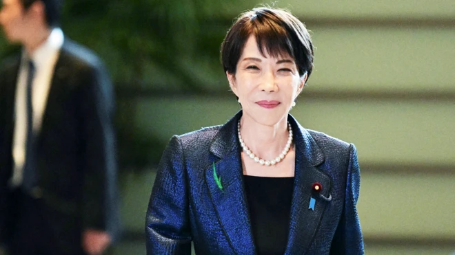 高市早苗身穿深藍色西裝外套，面帶笑容步行