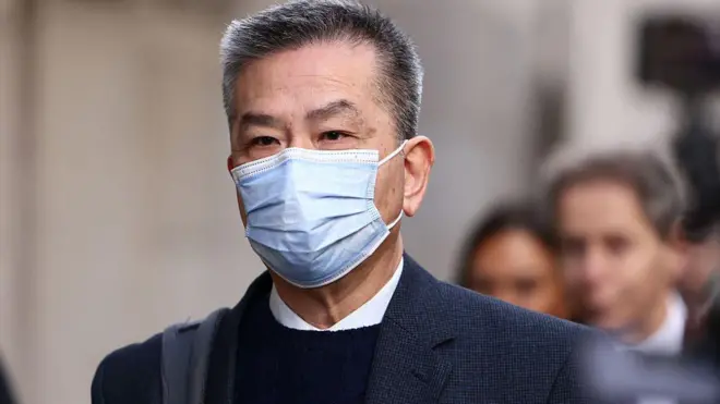 袁松彪抵達倫敦中央刑事法院。他留有短灰髮，佩戴藍色外科口罩遮住臉部下半部，身穿深色外套，內搭黑色針織上衣與白色有領襯衫