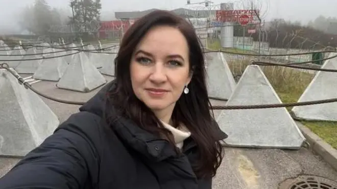 Премьер-министр Литвы Инга Ругинине в черной куртке делает селфи на фоне пограничных ограждений, за которыми начинается Беларусь