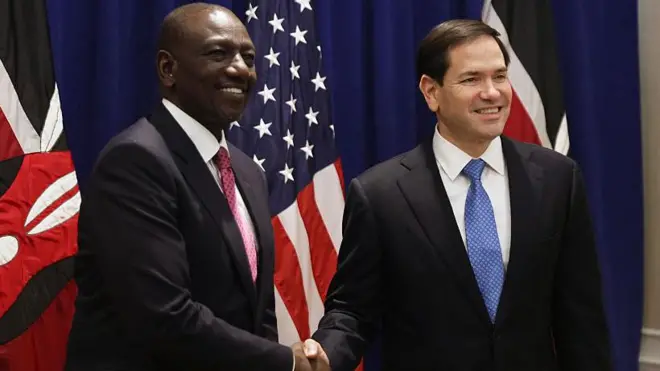 US Secretary of State Marco Rubio (R) and Kenya president William Ruto (L) dey shake hands wit Kenyan and di US flags wey dey for background
