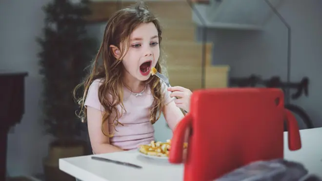 Young girl eating dinner watching tablet