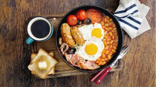 Refeição com pão, ovos, feijão, carne e outros alimentos com uma xícara de café