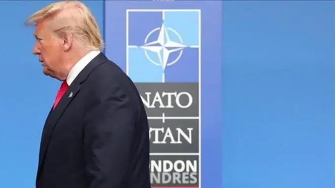 Дональд Трамп в анфас на тлі плакату з написом НАТО