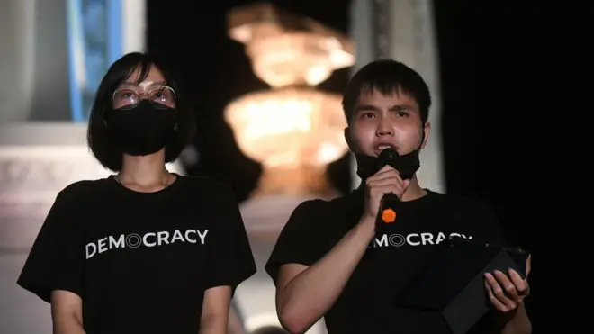 ทัตเทพ เรืองประไพกิจ เลขาธิการกลุ่มเยาวชนปลดแอก สวมเสื้อที่ทางกลุ่มทำขายเพื่อระดมทุน ถือไมโครโฟนสื่อสารกับผูุ้ชุมนุมที่อนุสาวรีย์ประชาธิปไตยคืนวันที่ 18 ก.ค.