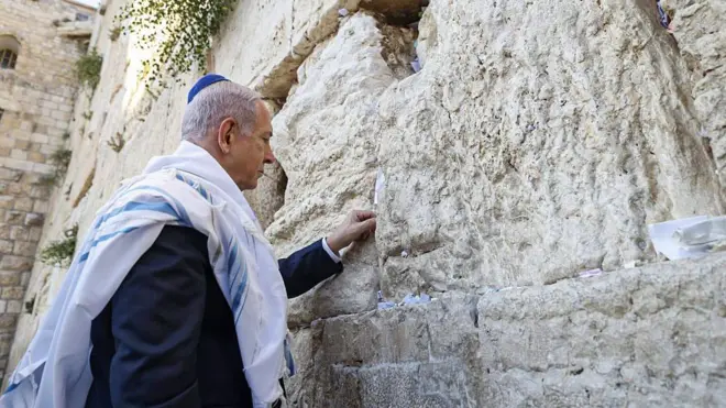 رئيس الوزراء الإسرائيلي، بنيامين نتنياهو، أمام حائط البراق/المبكى في القدس في 12 يونيو/حزيران 2025، يضع ورقة  مكتوب عليها آية من الكتاب المقدس "هو ذا شعب يقوم كلبؤة، ويرتفع كأسد" (سفر العدد 24:23)
