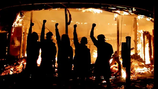 Protesters are seen outside of a liquor store on fire