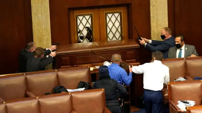 Охоронці Конгресу дістали зброї і ціляться убік дверей, які штурмували прихильники Трампа.