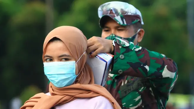 Seorang personel TNI AD memasangkan masker kepada warga yang terjaring razia kepatuhan penggunaan masker di Taman Digulis, Pontianak, Kalimantan Barat, Minggu (12/07).