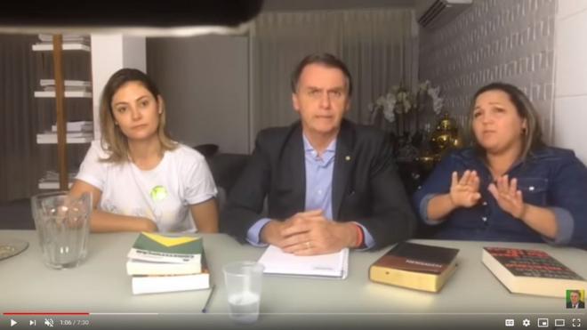 Reprodução de transmissão ao vivo feita por Bolsonaro, em que aparece ao lado da esposa e de intérprete de libras