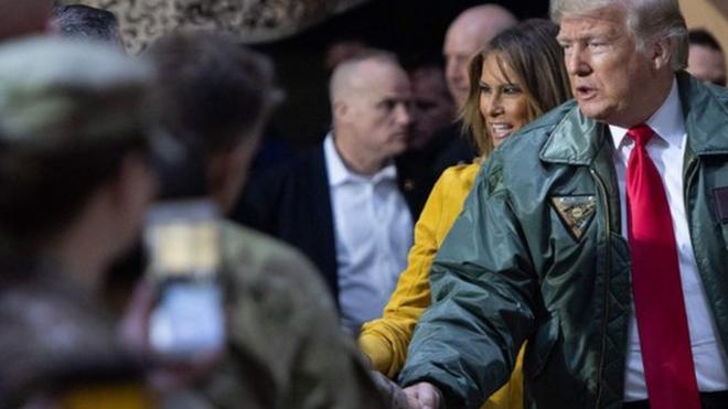 特朗普身穿绿色外衣、佩带着写有"三军统帅"名牌，与驻伊拉克美军握手。