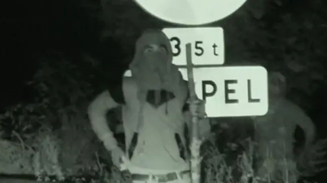 Un traficante de personas armado con un palo espera en la cuneta de la carretera principal de Calais, Francia