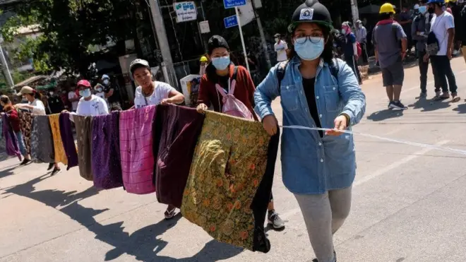 Women create a barrier across a street made of sarongs.