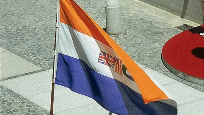 El expresidente sudafricano Pieter Willem Botha y su esposa Elize se paran frente al edificio del Parlamento en Ciudad del Cabo durante la apertura estatal del Parlamento en 1987. La bandera que flamea es la antigua insignia de la República de Sudáfrica, utilizada desde 1928-1994.